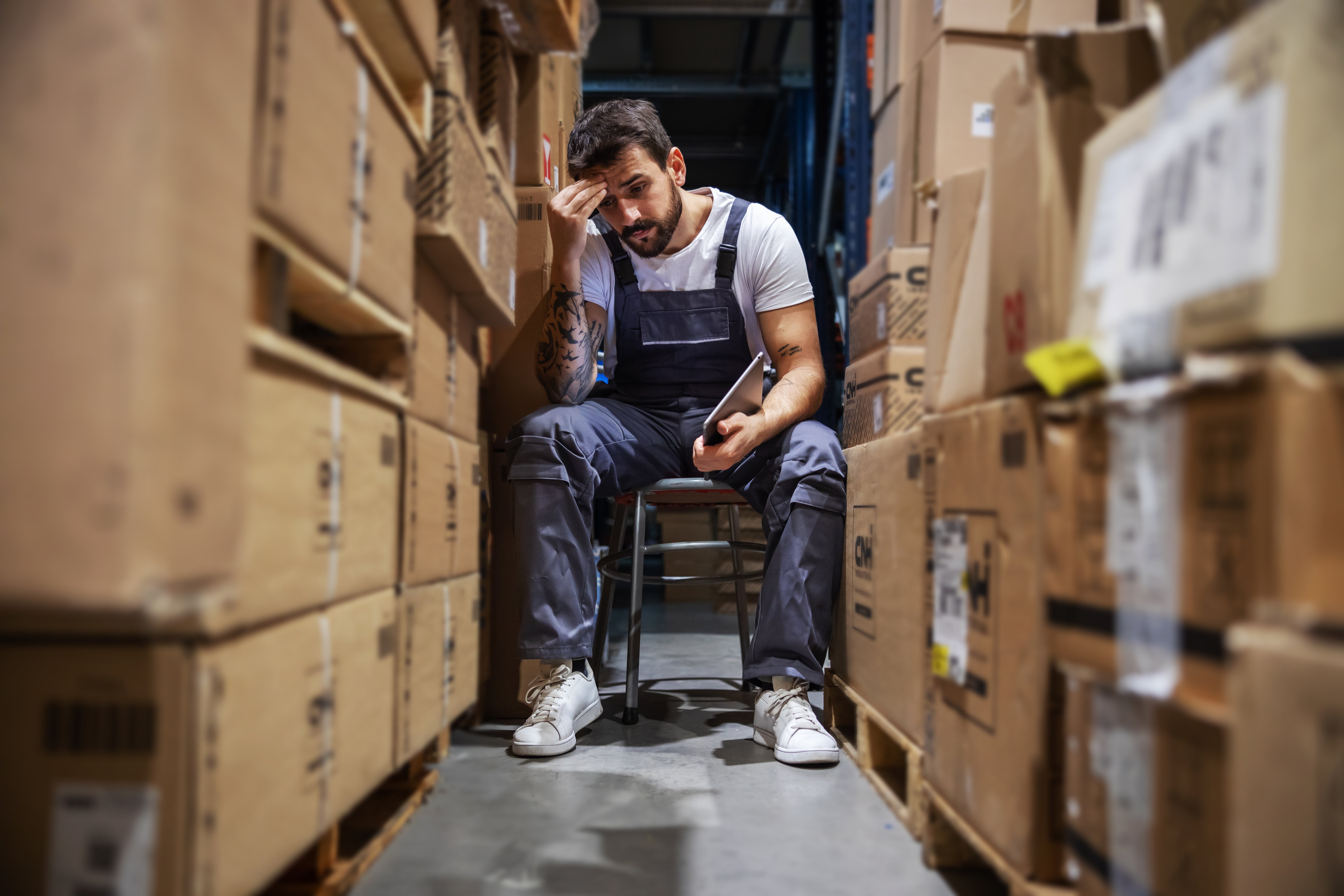 frustrated man sitting between stacks of boxes in a storage warehouse